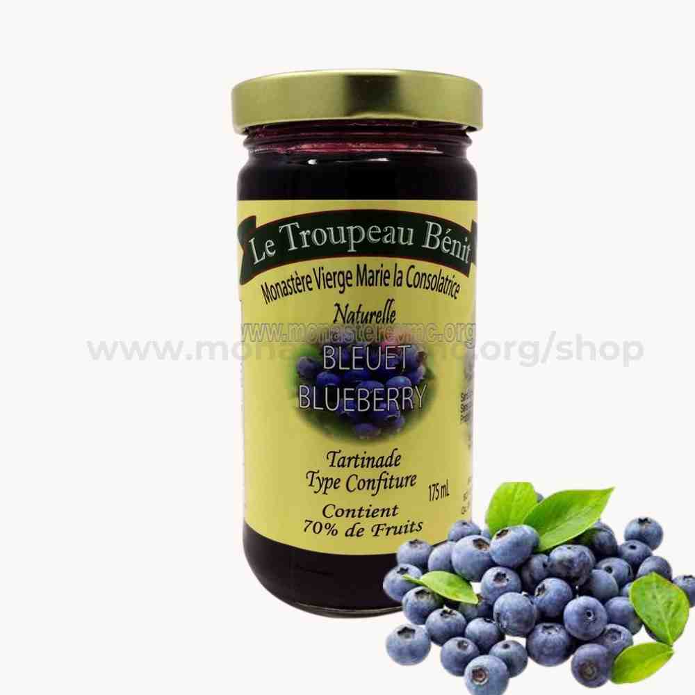 Jar of blueberry jam with a yellow label branded Le Troupeau Benit and blueberries on a white background