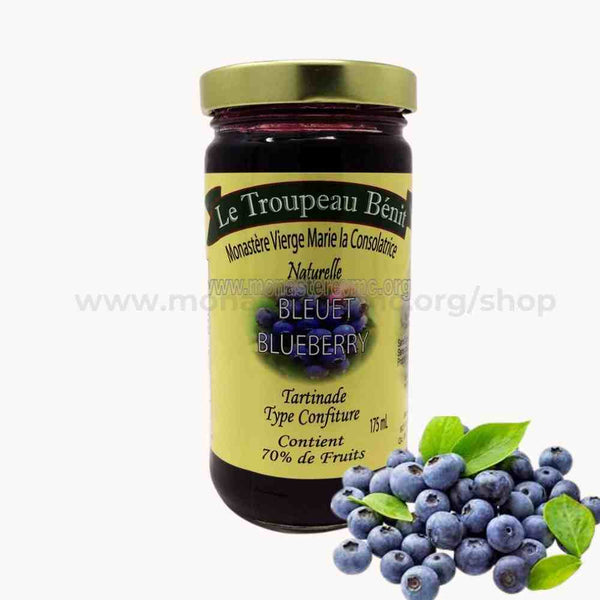 Jar of blueberry jam with a yellow label branded Le Troupeau Benit and blueberries on a white background