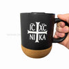 Black mug with cork base featuring a white cross and text on a white background sold by the sisters of monasterevmc.org