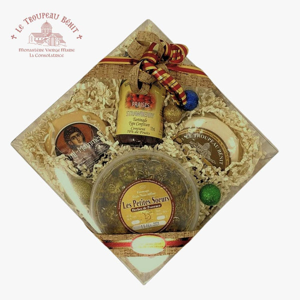 A gift box of local made cheeses and from Le Troupeau Benit, arranged in a diamond orientation on a white background. The box contains several round and oval cheeses wrapped in white paper, a jar of jam, and a round container of fresh goat cheese balls, all nestled in white shredded paper and tied with red patterned ribbons.