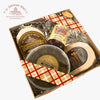 A gift box of gourmet cheeses and spreads from Le Troupeau Bénit, featuring Le Bon Berger cheese, Athonite, Les Petites Soeurs cheese, and mixed berries jam, arranged in a kraft box with a red and beige checkered ribbon on a white background.