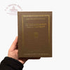 Brown book held by a hand with visible text and logo on a white background
