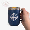Navy blue mug with white cross and text held by a hand on a white background