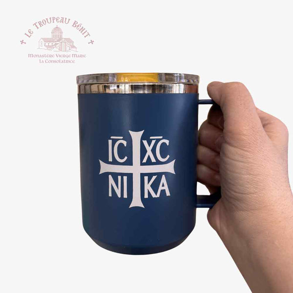 Navy blue mug with white cross and text held by a hand on a white background