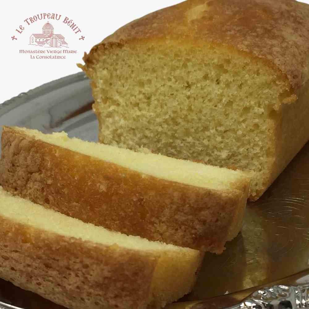 Loaf of lemon cake with a slice cut, on a metallic surface with 'Le Troupeau Bénit' branding.