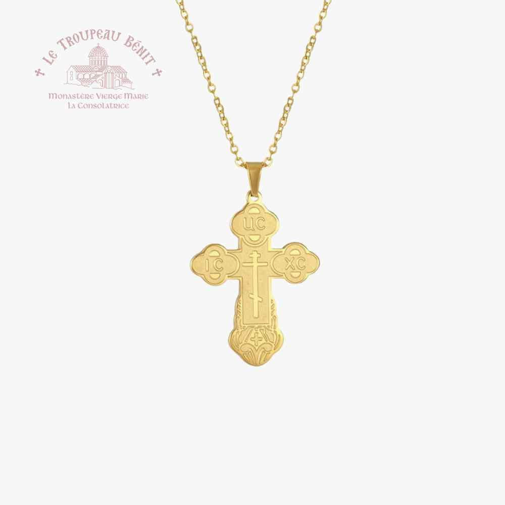 Gold cross pendant on a chain with 'Le Troupeau Bénit' logo in the corner.