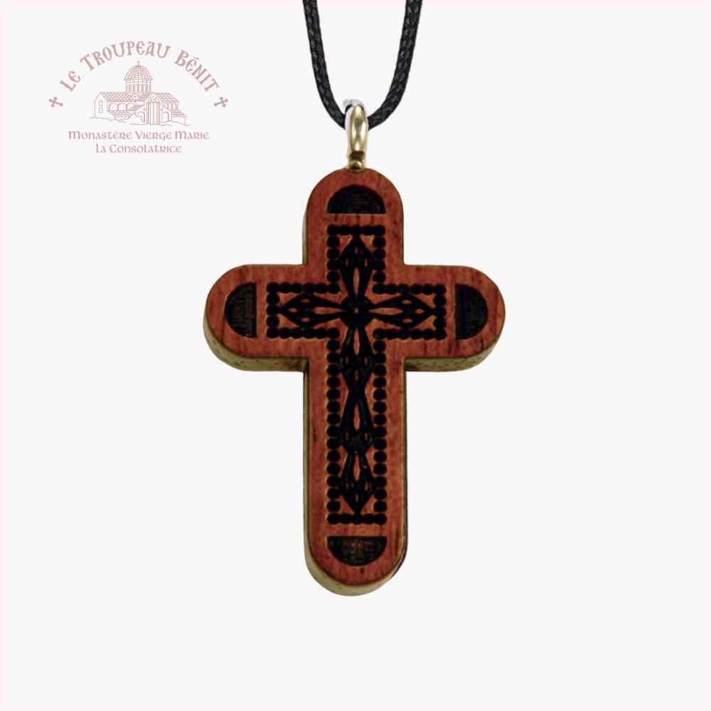Wooden cross pendant with intricate design on a white background, featuring the Le Troupeau Benit logo.