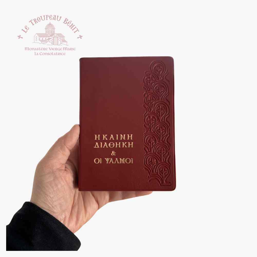 Red leather-bound book held in a hand with decorative embossing on a white background, featuring the logo of Le Troupeau Bénit.