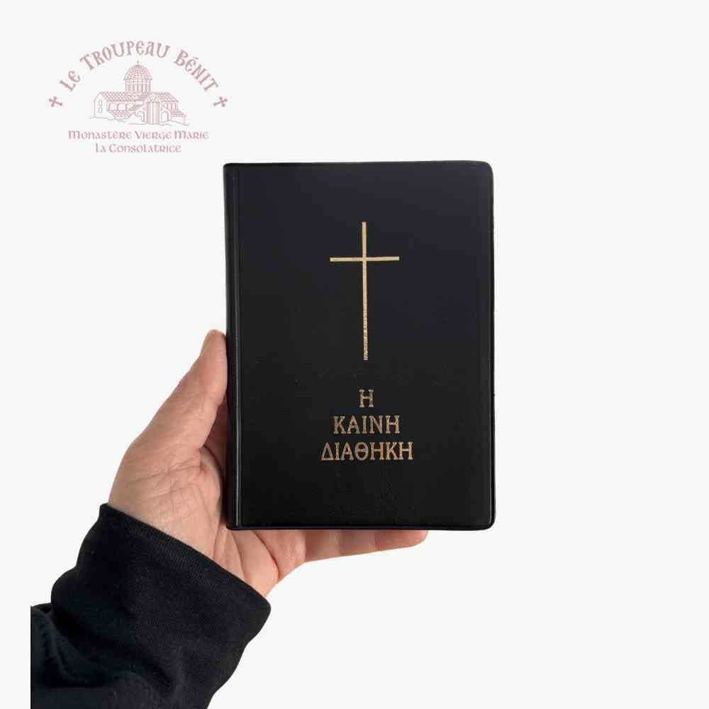 Black book with gold cross and text held by a hand on a white background, with Troupeau Benit logo in the corner.