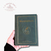 A hand holding a dark green hardcover book titled 'ΨΑΛΤΗΡΙΟΝ' with gold foil detailing, set against a plain white background with a Troupeau Benit logo watermark in the top left corner.