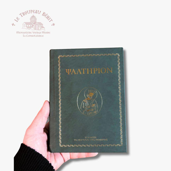 A hand holding a dark green hardcover book titled 'ΨΑΛΤΗΡΙΟΝ' with gold foil detailing, set against a plain white background with a Troupeau Benit logo watermark in the top left corner.