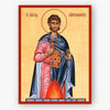 A religious icon print of Saint Aimilianos on a beige background with a red border, showing the saint in pink and blue robes holding a cross and book, with flames at the bottom.