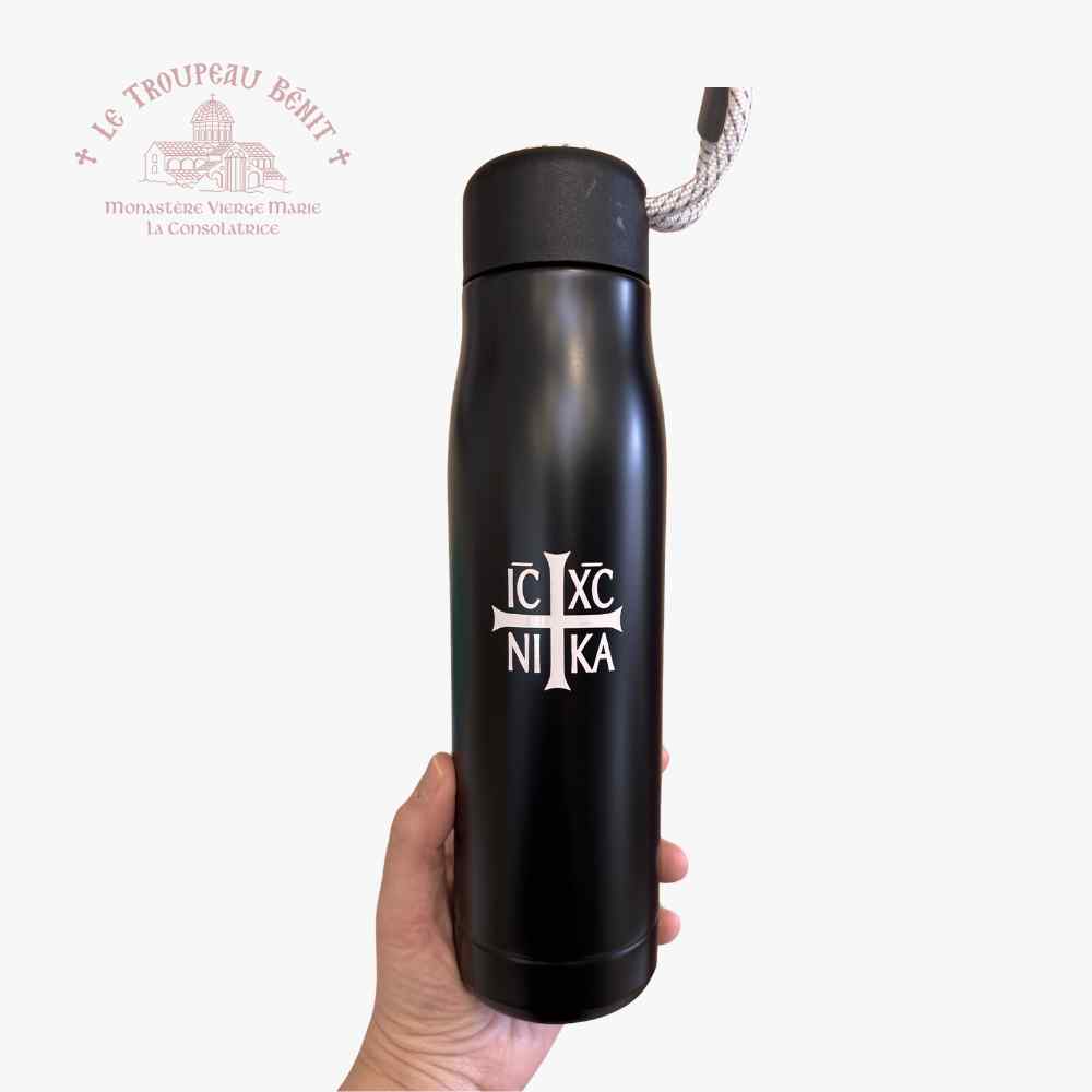 Black tall water bottle with IC XC NIKA emblem in white held by a hand and Le Troupeau Benit logo in top left corner