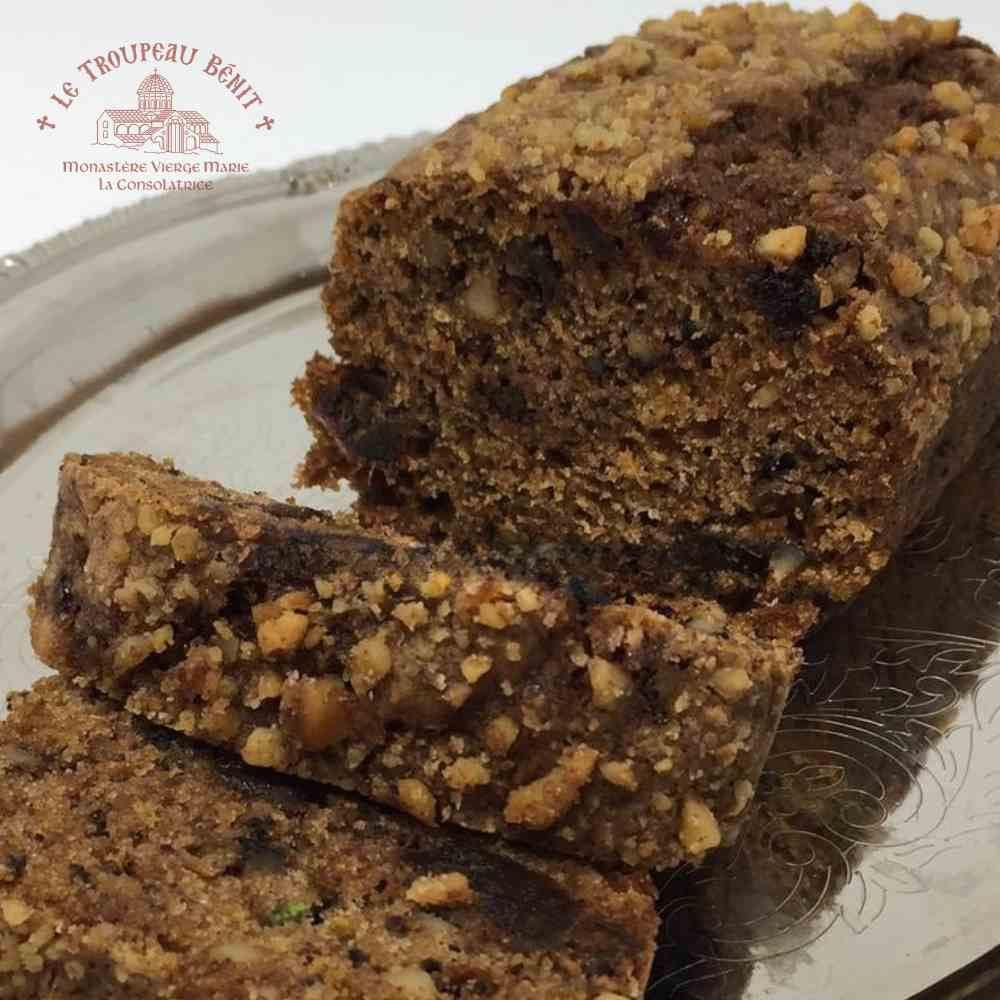 Loaf of wheat free fruit bread with a slice cut, on a decorative plate with 'Le Troupeau Bénit' branding.