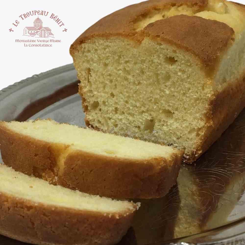 Loaf of lemon cake with a slice cut, displayed on a plate with 'Le Troupeau Bénit logo branding.
