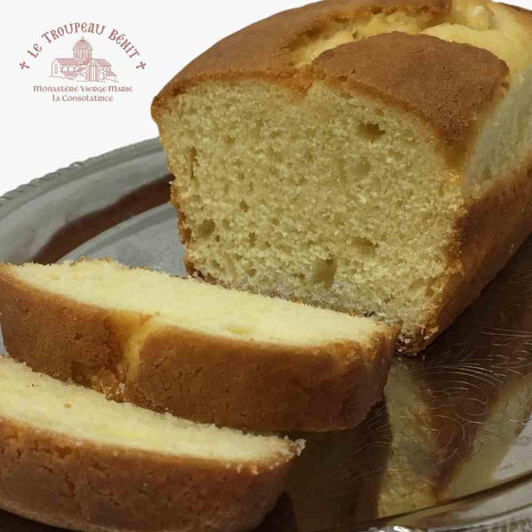 Loaf of lemon cake with a slice cut, displayed on a plate with 'Le Troupeau Bénit logo branding.